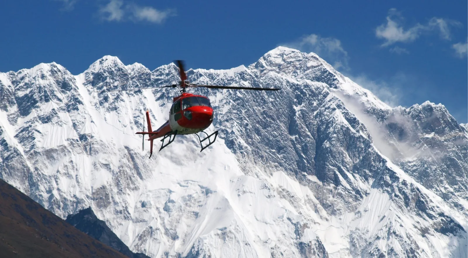 A red helicopter flying past the snow-covered Everest and Lhotse massif