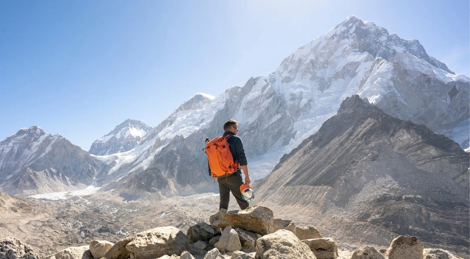 A trekker with an orange backpack looking out at the Everest range