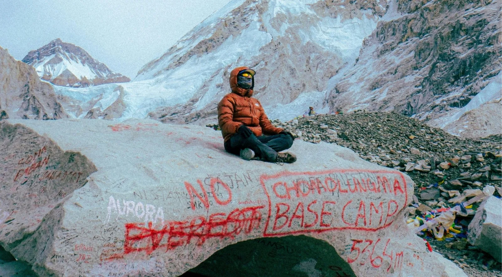 A trekker sitting on the Everest Base Camp marker rock at 5,364 meters