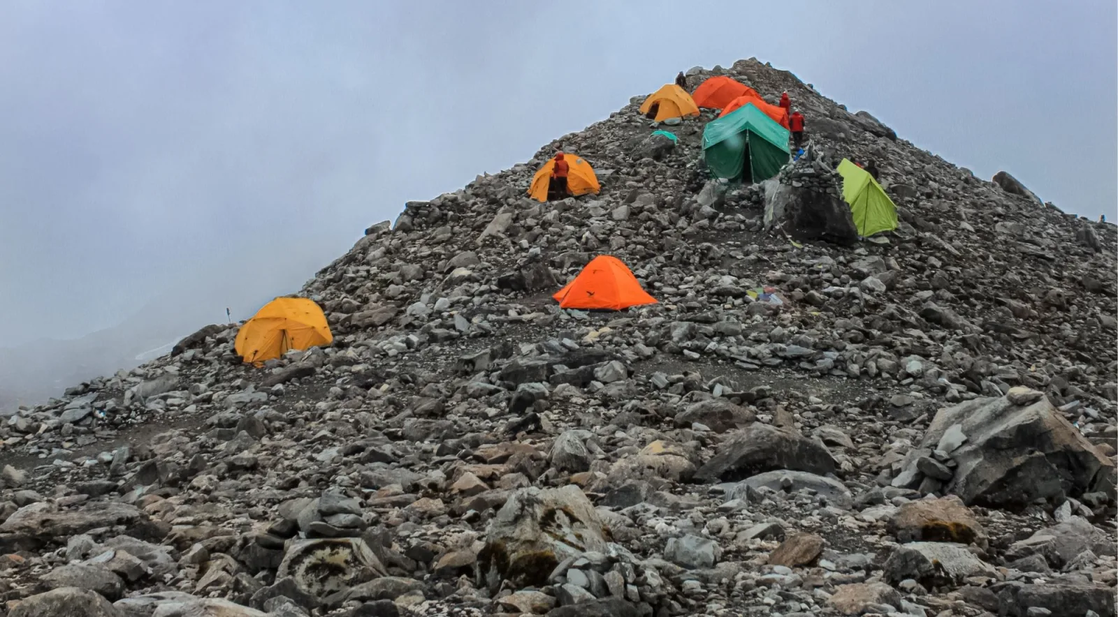 Colorful tents pitched on a rocky high-altitude camp in fog